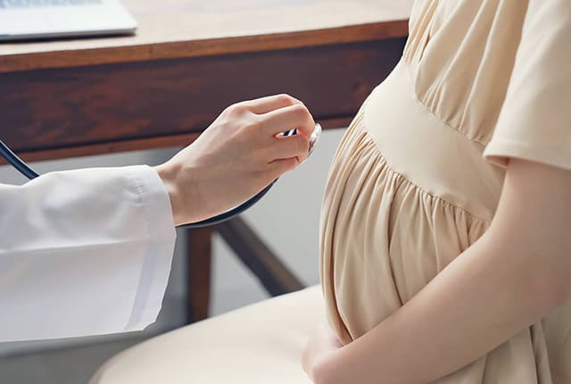 妊婦のお腹に聴診器を当てる医師の手元